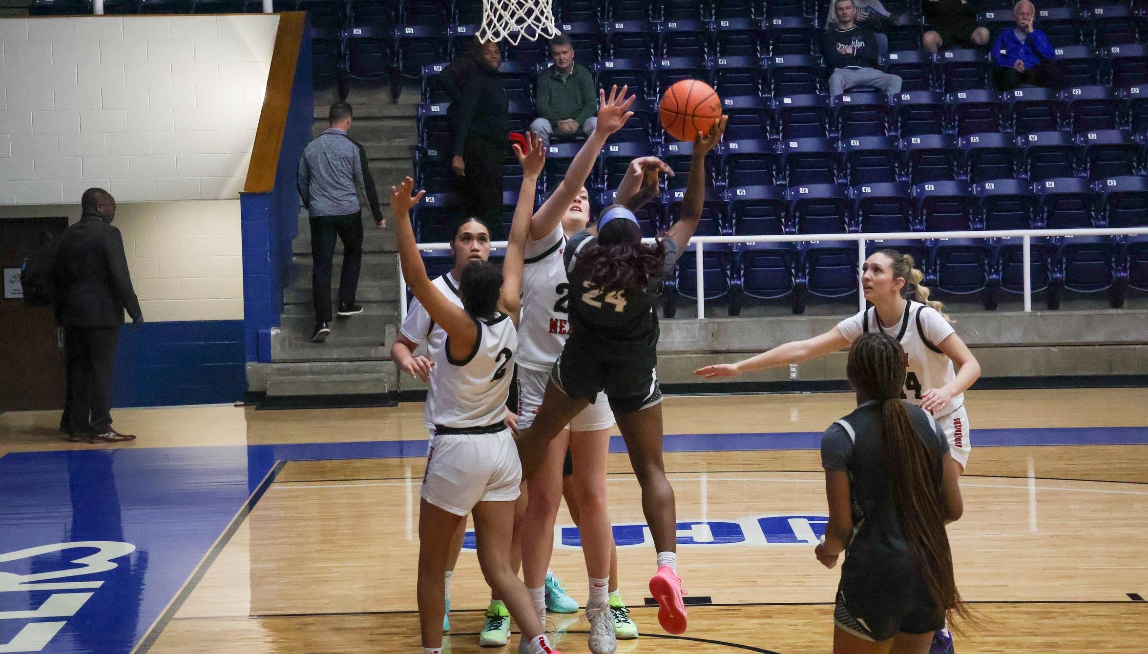 The basketball player in the navy jersey goes up for a basket with three defenders in white jerseys around her during a basketball game. 