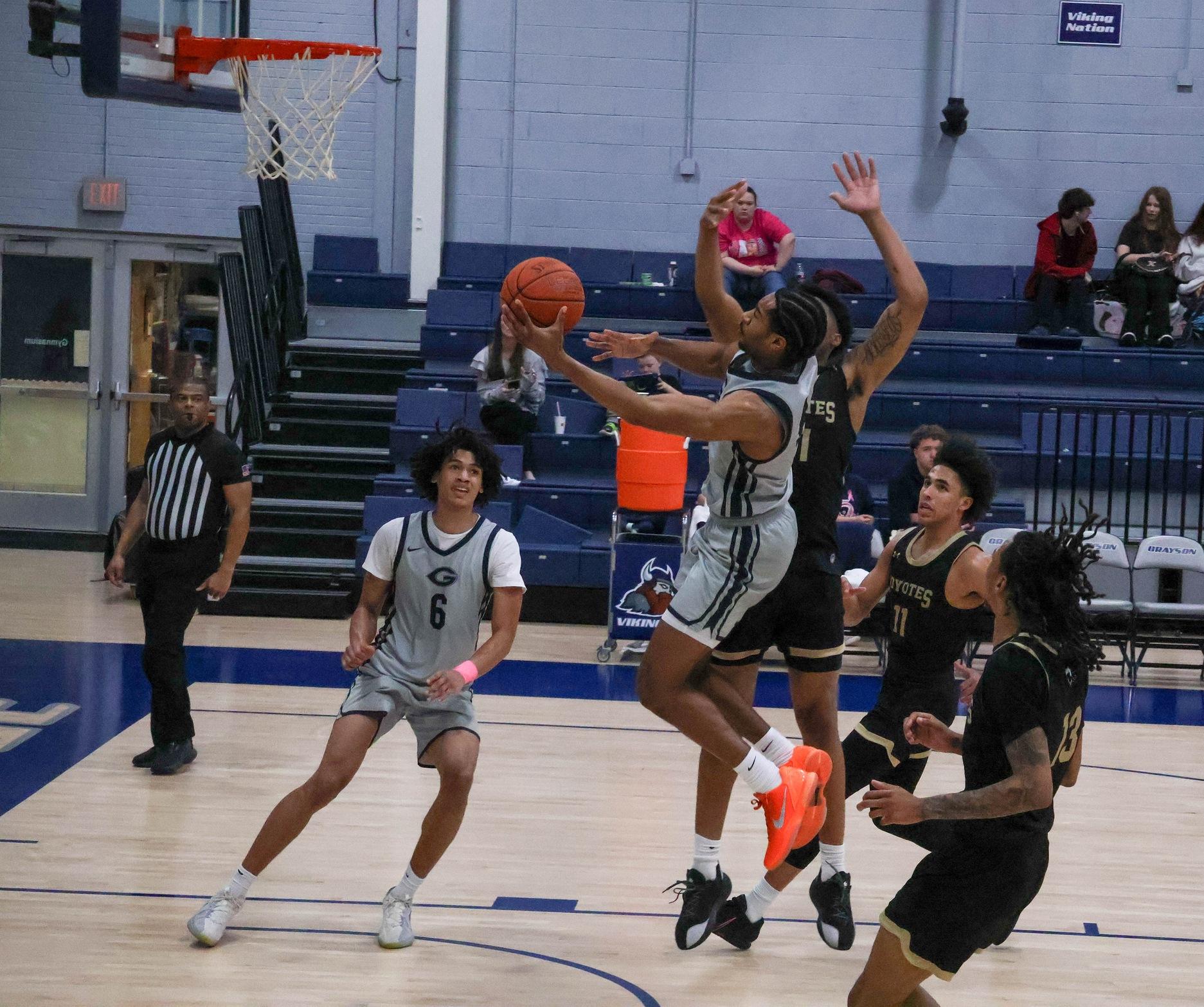 The Grayson Viking basketball player in the gray uniform drives to the basket. 